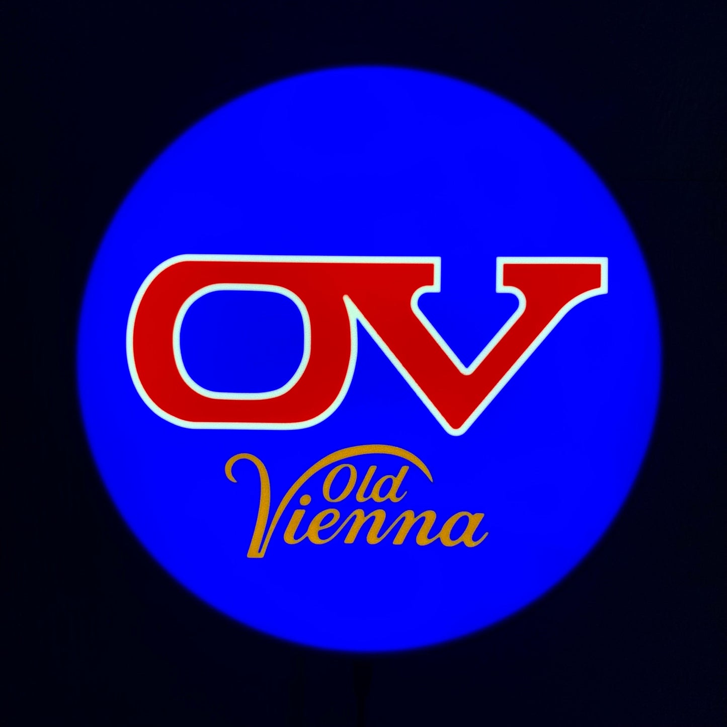 Logo of Old Vienna with red 'OV' and yellow 'Vienna' text on a blue circle on a led indoor sign against a black background.